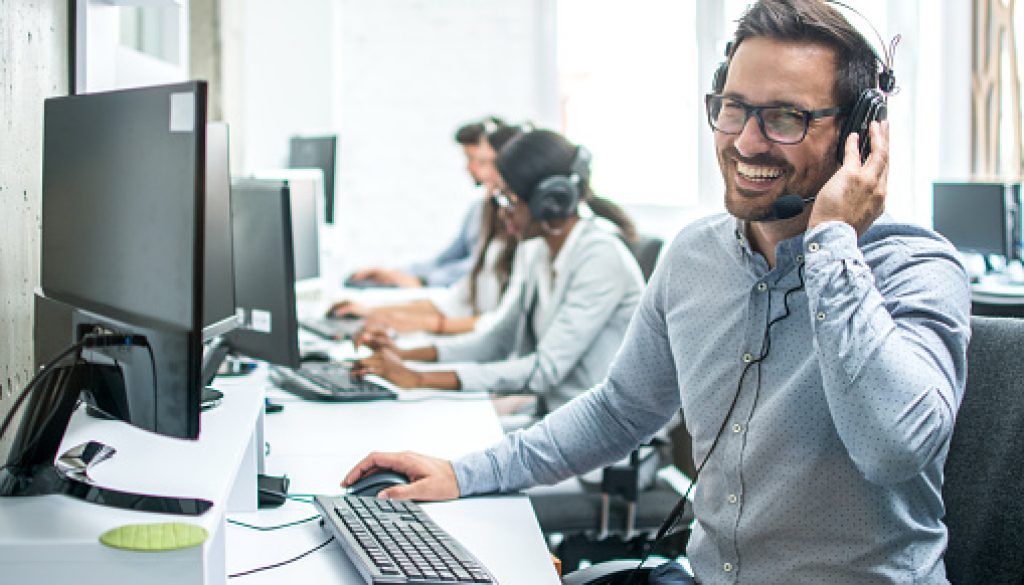Smiling handsome customer support operator with headset working in call center.